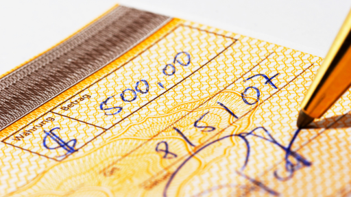 A Imagem mostra um cheque sendo prenchido a caneta simbolizando o pagamento da indenização. The image shows a check being written in pen, symbolizing the payment of compensation.